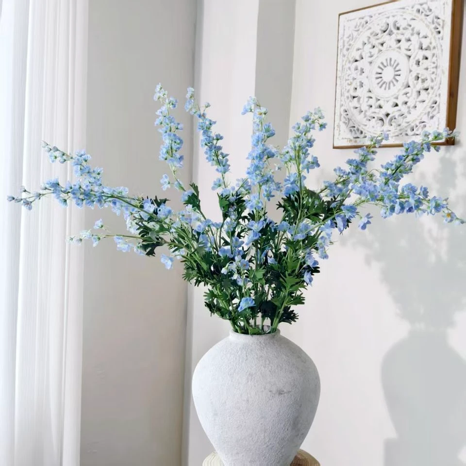 Blue and pale artificial delphinium sprays arranged in a white vase