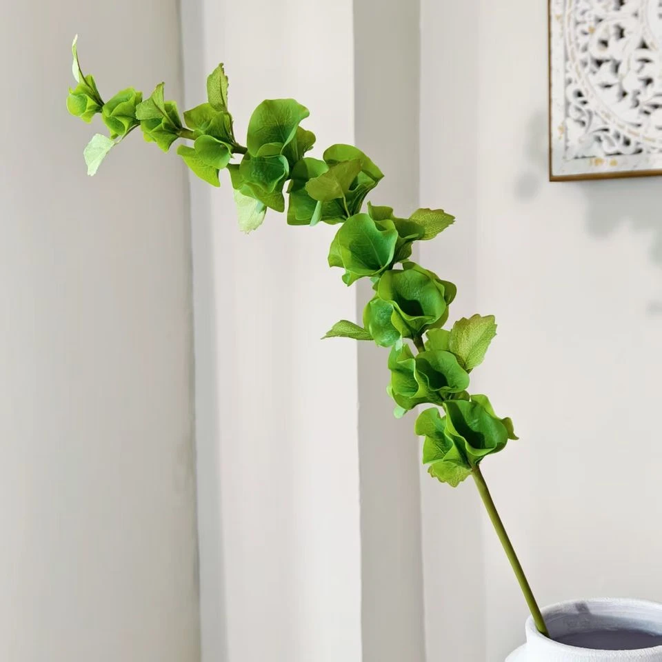 Green artificial Bells of Ireland stem displayed beside a small vase