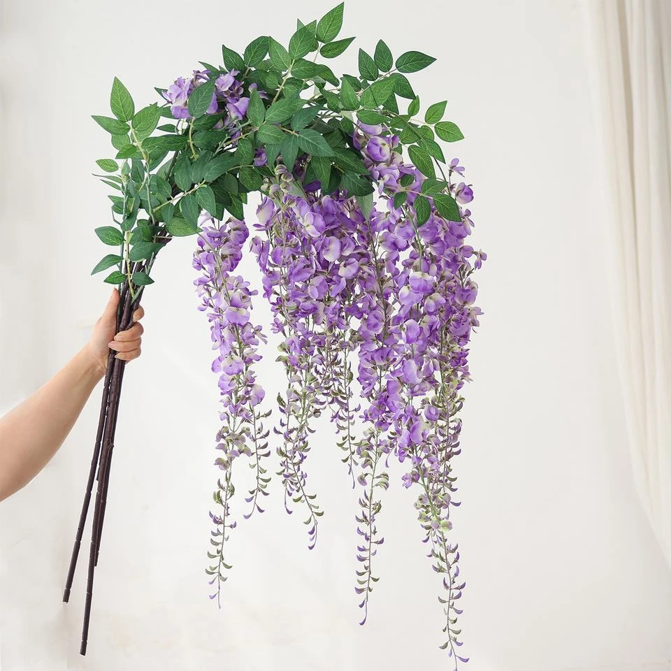Purple and white artificial wisteria clusters hanging from leafy branches held by the stems